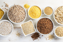 Selection of whole grains in white bowls - rice, oats, buckwheat, bulgur, porridge, barley, quinoa, amaranth,